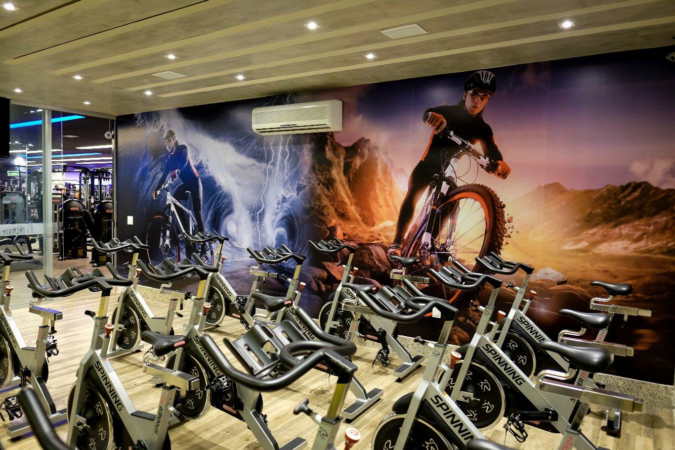 Sala de spinning da Fit One com bikes profissionais e painel gráfico